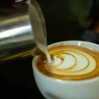 Pichet à lait en inox dessinant une rosace de latte art dans une tasse de café