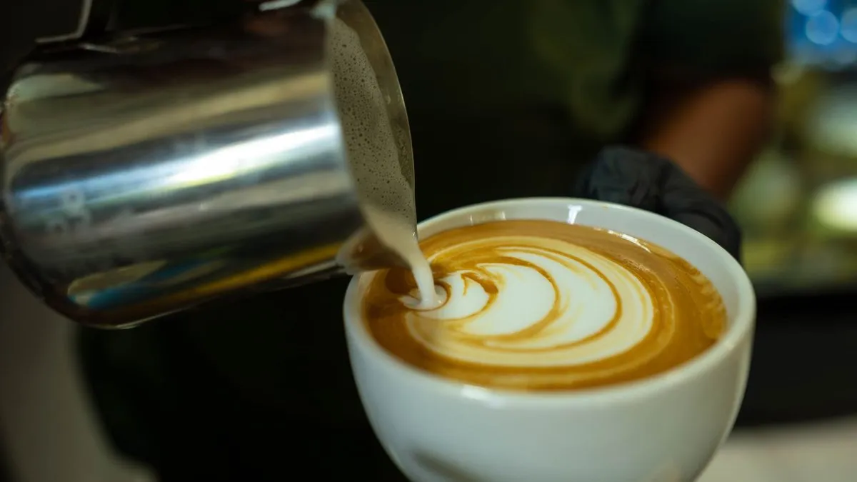 Pichet à lait en inox dessinant une rosace de latte art dans une tasse de café