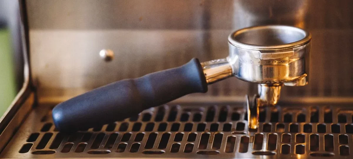 Porte-filtre en inox engagé sur une machine à café expresso, au-dessus de la grille d'égouttage