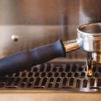 Porte-filtre en inox engagé sur une machine à café expresso, au-dessus de la grille d'égouttage