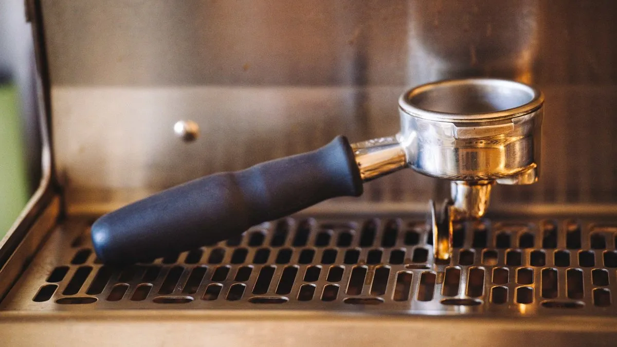 Porte-filtre en inox engagé sur une machine à café expresso, au-dessus de la grille d'égouttage