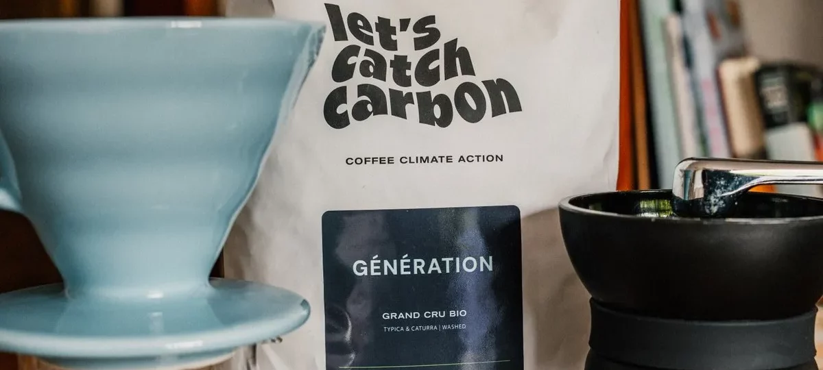 Sachet de café en grains bio let's catch carbon Génération à côté d'un dripper et d'un moulin à café manuel