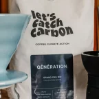 Sachet de café en grains bio let's catch carbon Génération à côté d'un dripper et d'un moulin à café manuel