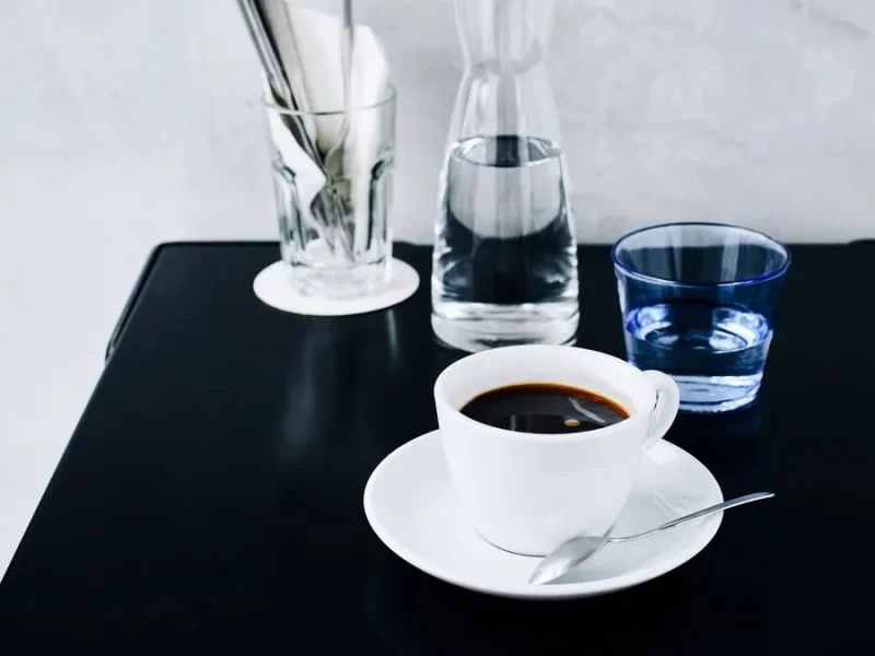 Tasse de café americano noir sur soucoupe à côté d'une carafe d'eau, sur une table noire