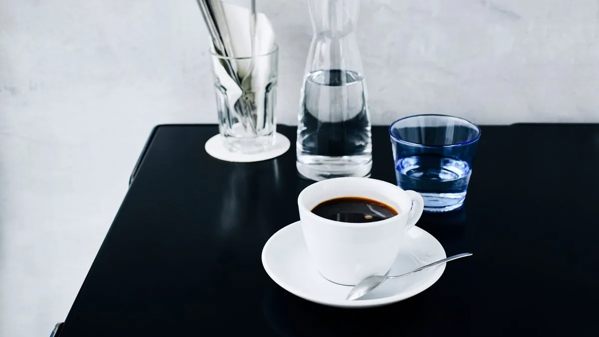 Tasse de café americano noir sur soucoupe à côté d'une carafe d'eau, sur une table noire