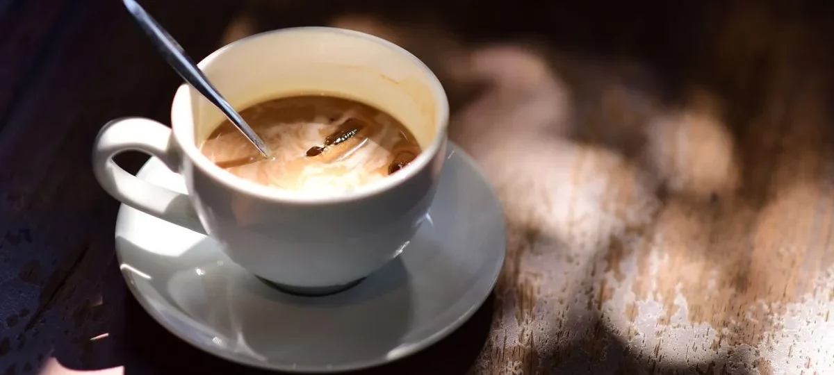 Tasse de café au lait avec une cuillère sur une table en bois, lumière chaude
