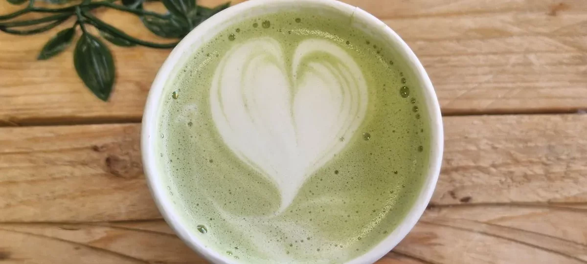 Tasse de matcha latte avec un cœur en mousse de lait, vue de dessus sur une table en bois