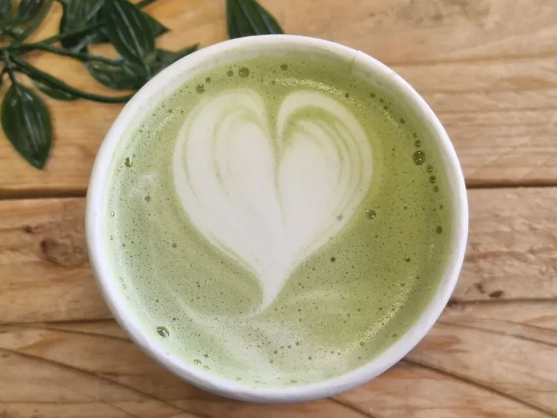 Tasse de matcha latte avec un cœur en mousse de lait, vue de dessus sur une table en bois