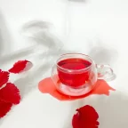 Tasse en verre d'infusion d'hibiscus rouge entourée de fleurs d'hibiscus fraîches sur fond blanc