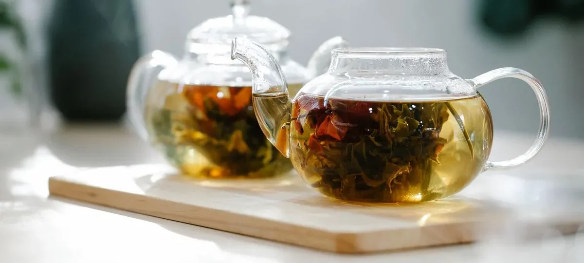 Thé en feuilles infusant dans deux théières en verre posées sur une planche en bois