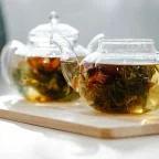Thé en feuilles infusant dans deux théières en verre posées sur une planche en bois