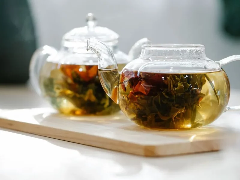 Thé en feuilles infusant dans deux théières en verre posées sur une planche en bois