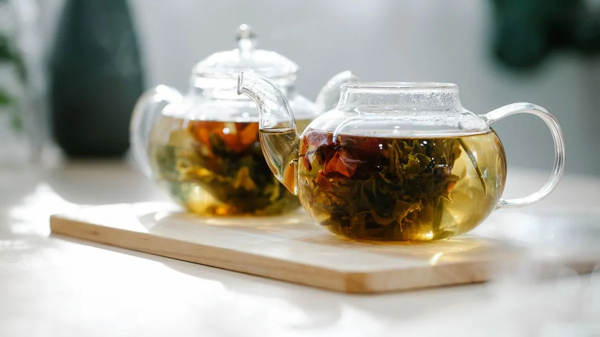 Thé en feuilles infusant dans deux théières en verre posées sur une planche en bois